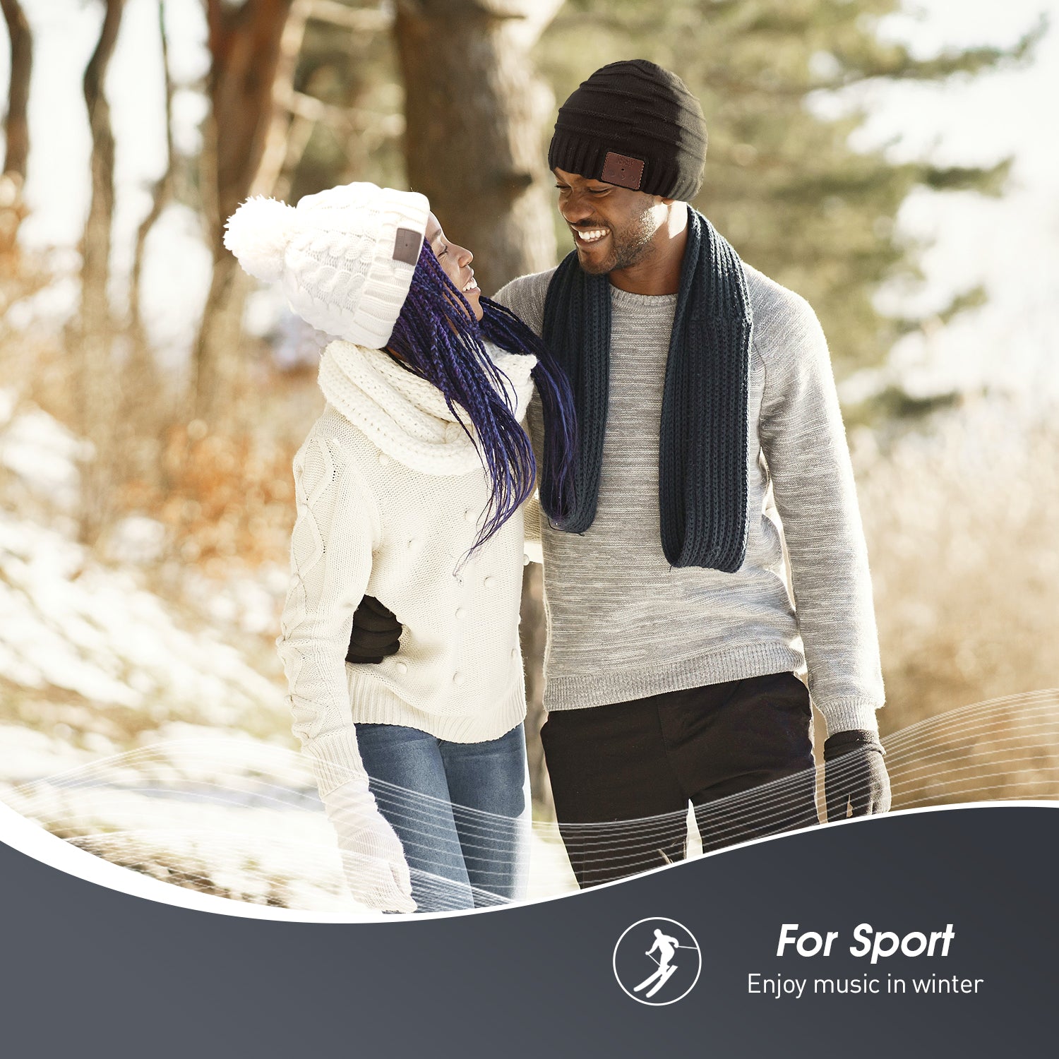 On a snowy hillside, a woman wears a white beanie with full bobble on top. A man wears a black beanie